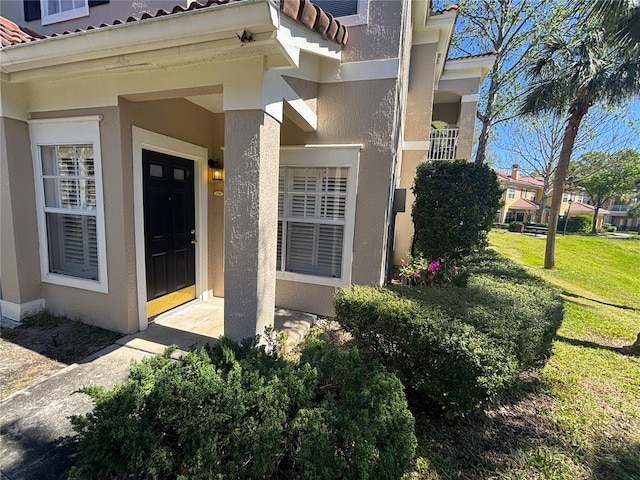 entrance to property featuring stucco siding, a lawn, and a tile roof