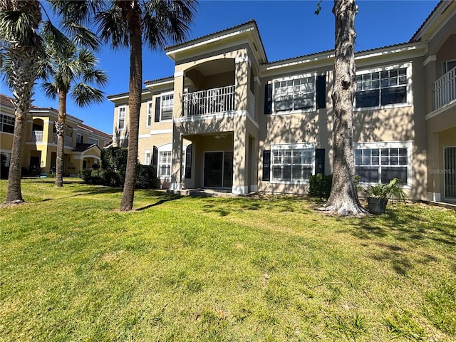 back of property with a balcony, stucco siding, and a yard