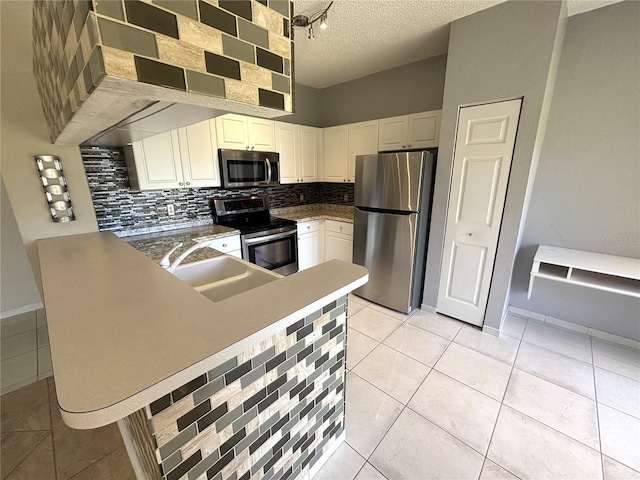 kitchen with light tile patterned flooring, a sink, appliances with stainless steel finishes, a textured ceiling, and backsplash