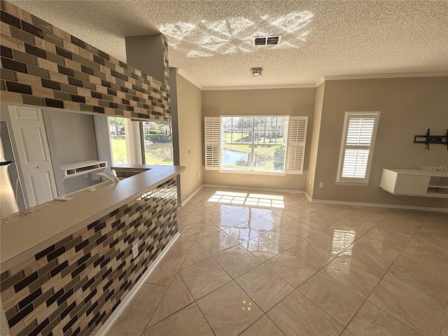 kitchen with visible vents, baseboards, a textured ceiling, and crown molding