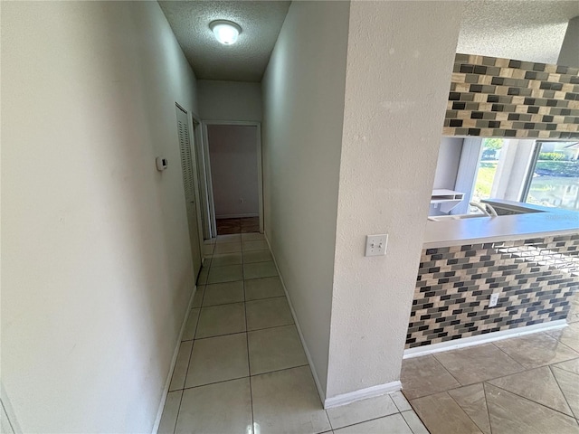 hallway featuring tile patterned flooring, a textured ceiling, and baseboards