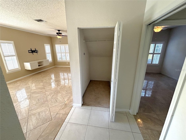 hallway with light tile patterned floors, visible vents, baseboards, and a textured ceiling