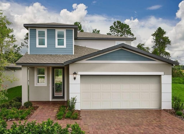 view of front of property with an attached garage, decorative driveway, roof with shingles, and stucco siding