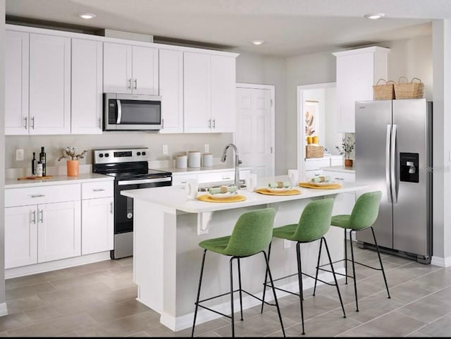 kitchen with a center island with sink, a sink, light countertops, appliances with stainless steel finishes, and white cabinetry