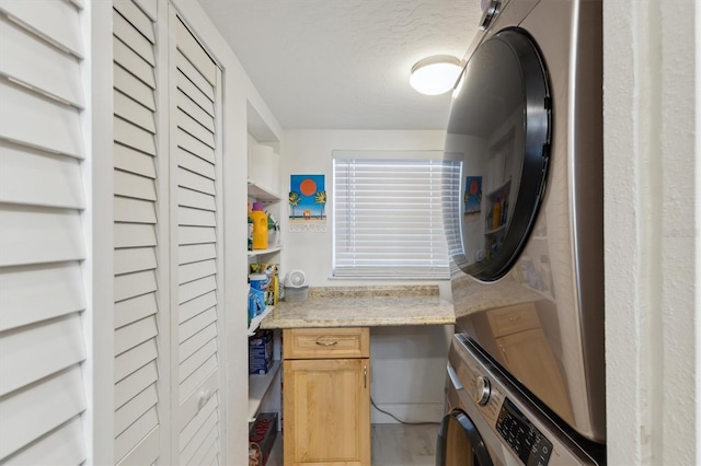 washroom featuring cabinet space, stacked washer and clothes dryer, and a textured ceiling