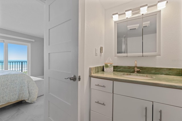 ensuite bathroom featuring vanity, a textured wall, marble finish floor, and connected bathroom