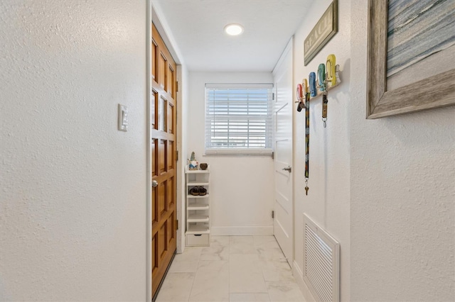 hall featuring visible vents, marble finish floor, baseboards, and a textured wall