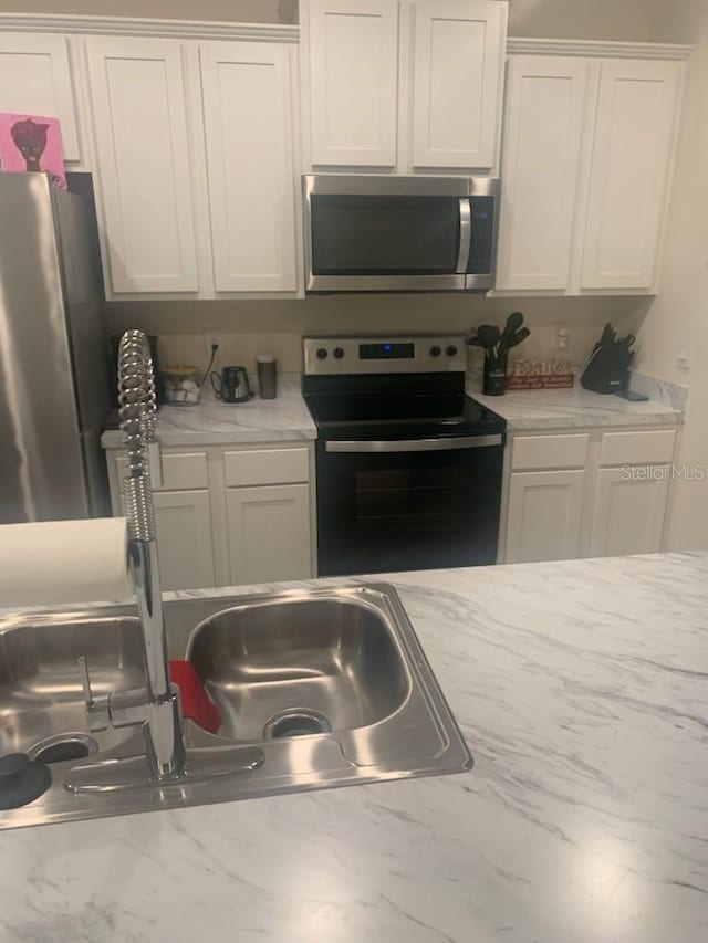 kitchen with white cabinets, light stone counters, and appliances with stainless steel finishes