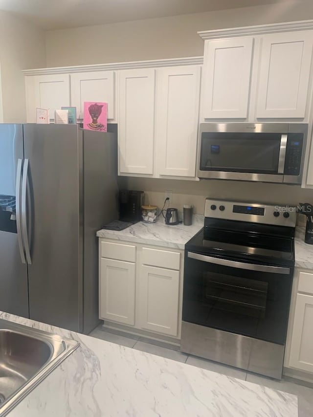 kitchen featuring light stone counters, a sink, stainless steel appliances, white cabinets, and marble finish floor