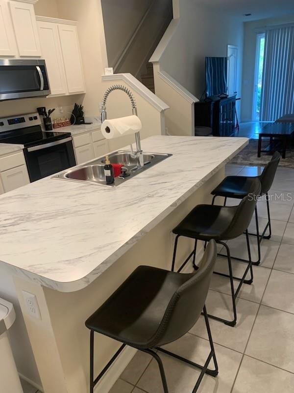 kitchen featuring light tile patterned floors, appliances with stainless steel finishes, a kitchen breakfast bar, white cabinets, and a sink