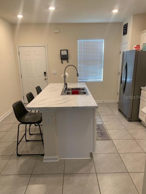 kitchen featuring white cabinets, light tile patterned floors, stainless steel fridge, and a sink