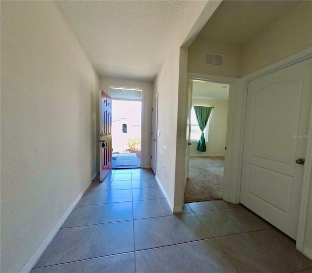 corridor featuring light tile patterned floors, visible vents, a textured ceiling, and baseboards