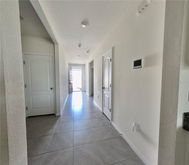 corridor with tile patterned flooring, baseboards, and a textured ceiling