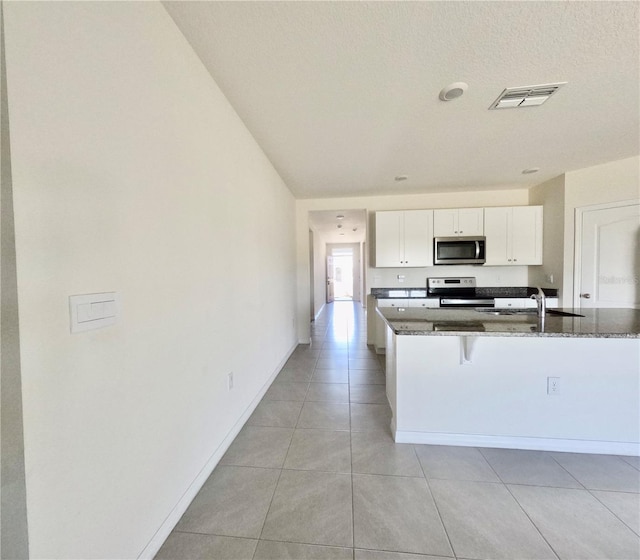 kitchen featuring visible vents, white cabinetry, stainless steel appliances, and dark stone counters