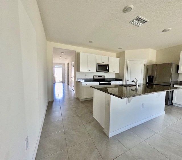 kitchen featuring dark stone countertops, a center island with sink, visible vents, a sink, and stainless steel appliances