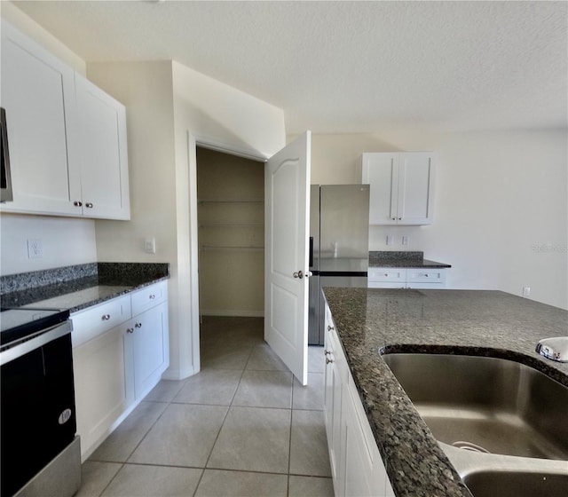 kitchen with range with electric cooktop, a sink, freestanding refrigerator, dark stone counters, and white cabinets