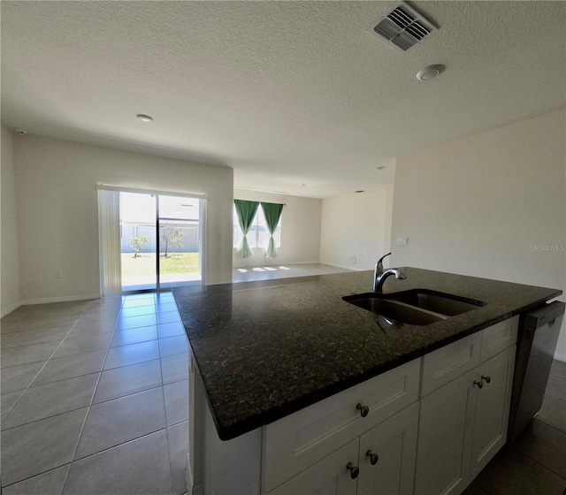 kitchen featuring dark stone countertops, light tile patterned floors, visible vents, a sink, and open floor plan