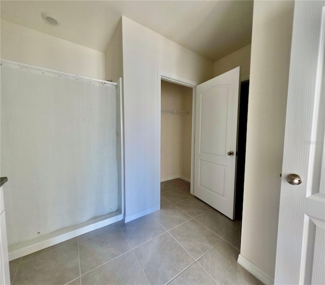 interior space featuring tile patterned flooring, a walk in closet, a shower with curtain, and baseboards