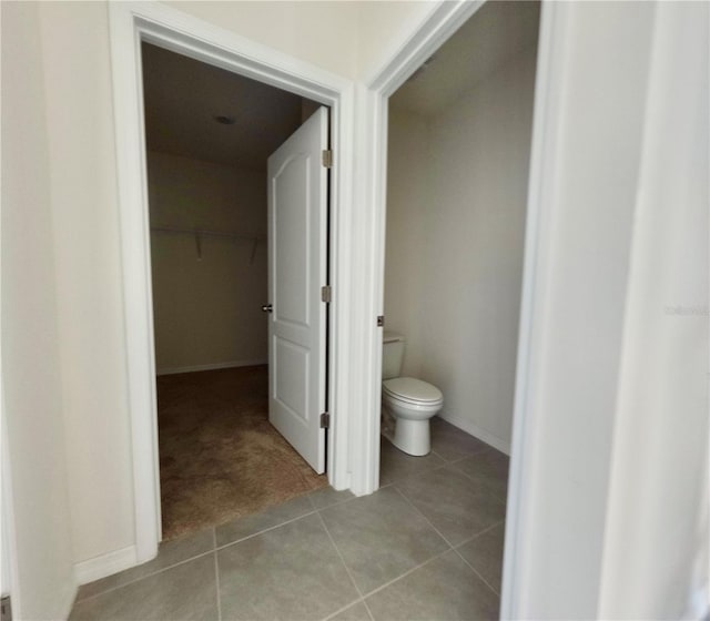 bathroom featuring a walk in closet, baseboards, toilet, and tile patterned flooring