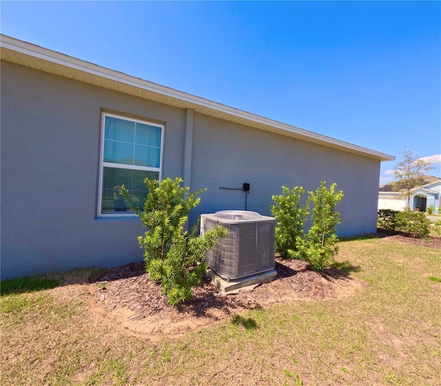 exterior space with stucco siding, a lawn, and central AC