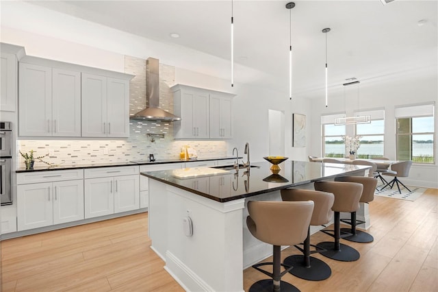 16689 Broadwater Ave, Winter Garden, FL 34787 - kitchen with a sink, tasteful backsplash, light wood-style floors, wall chimney range hood, and an island with sink