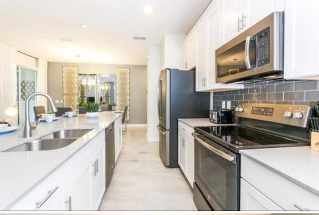 kitchen with appliances with stainless steel finishes, white cabinetry, light countertops, and a sink