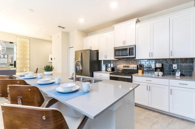 kitchen with a sink, stainless steel appliances, tasteful backsplash, and white cabinetry