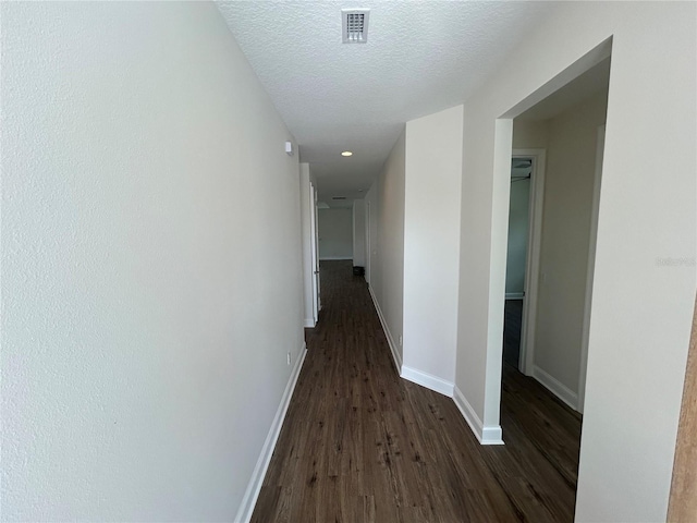 hallway featuring visible vents, dark wood-style floors, baseboards, and a textured ceiling
