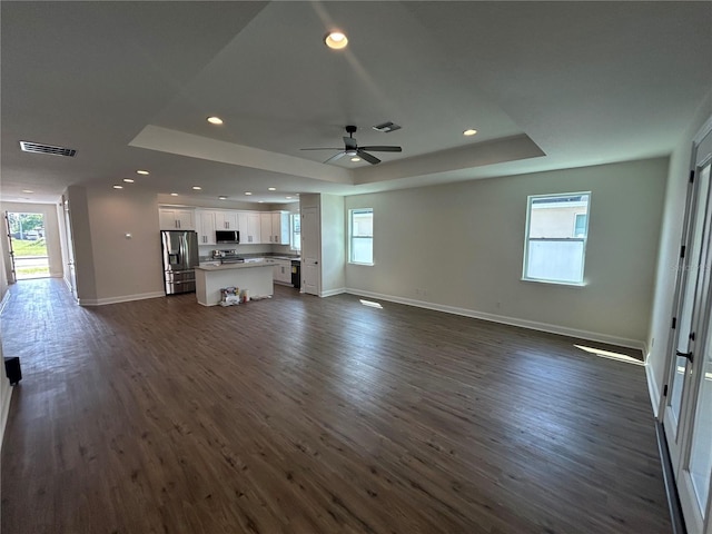 unfurnished living room with a wealth of natural light, a tray ceiling, visible vents, and dark wood finished floors