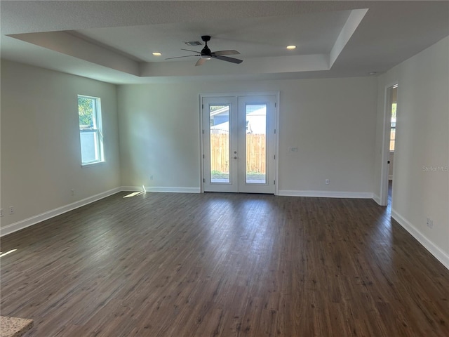 spare room featuring a tray ceiling, baseboards, and dark wood-style floors