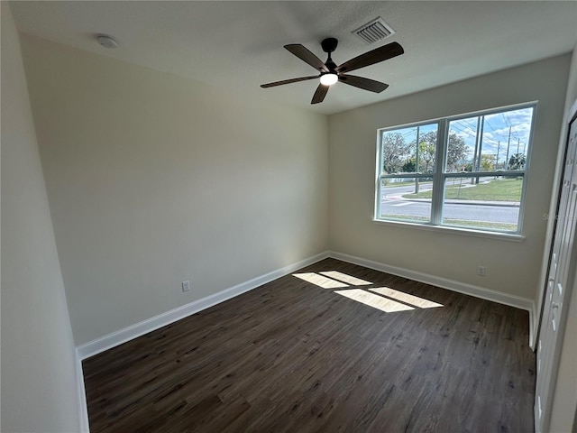 empty room featuring visible vents, ceiling fan, baseboards, and dark wood-style flooring