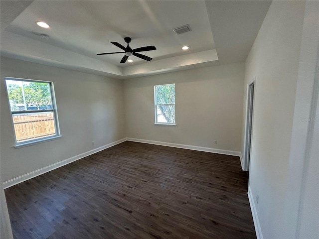 spare room with visible vents, a raised ceiling, baseboards, and dark wood-style flooring