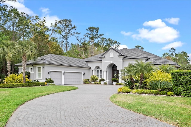 view of front of home with a front lawn, stucco siding, curved driveway, and an attached garage