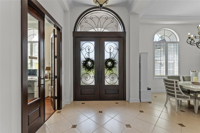 entryway with light tile patterned floors, french doors, baseboards, a chandelier, and ornamental molding