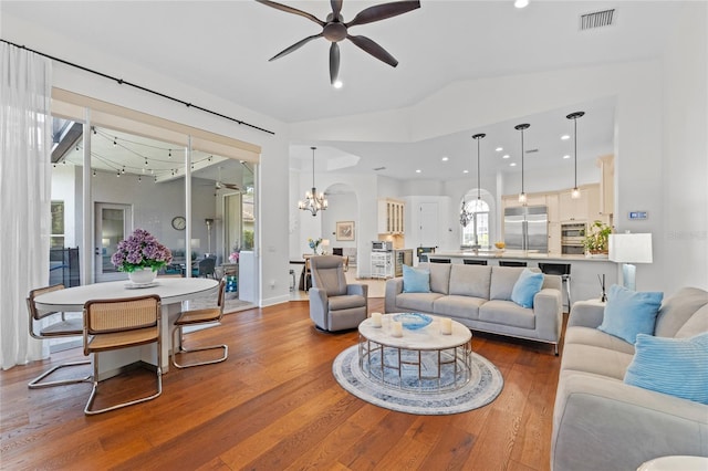 living area with ceiling fan with notable chandelier, wood finished floors, visible vents, recessed lighting, and vaulted ceiling