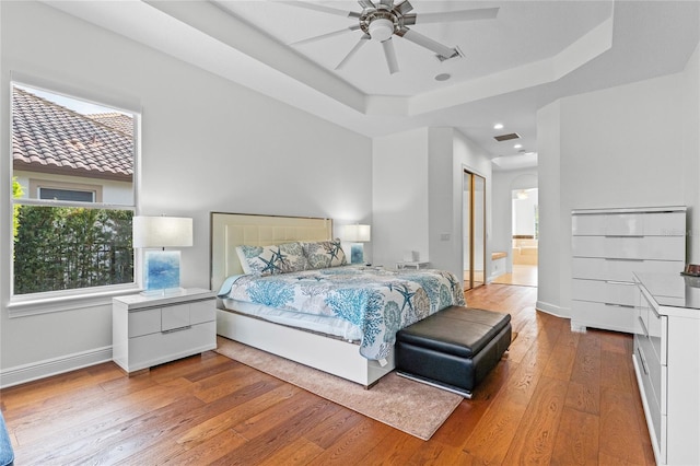 bedroom with a tray ceiling, visible vents, baseboards, and wood-type flooring