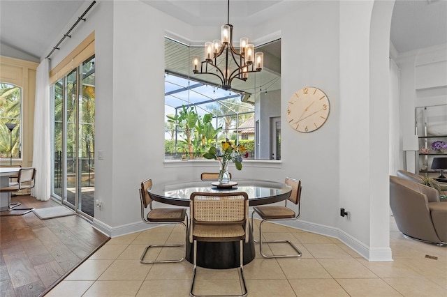 tiled dining area with baseboards, a sunroom, a chandelier, and arched walkways