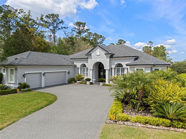 view of front of house with an attached garage, a tiled roof, stucco siding, a front lawn, and decorative driveway