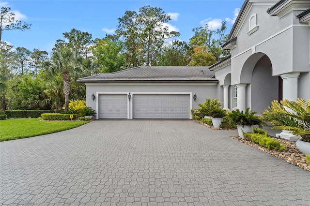 exterior space with a yard, a garage, stucco siding, a tiled roof, and decorative driveway