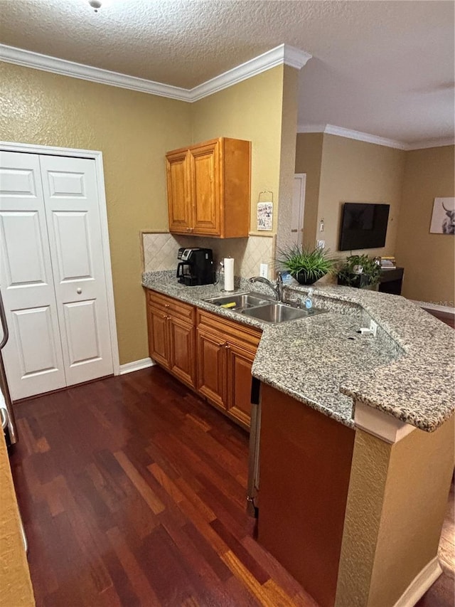 kitchen with light stone counters, brown cabinetry, dark wood finished floors, a peninsula, and a sink