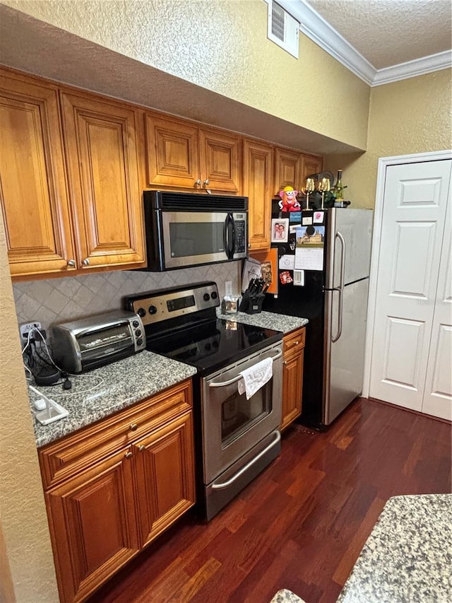 kitchen with ornamental molding, brown cabinets, a textured wall, stainless steel appliances, and dark wood-style flooring