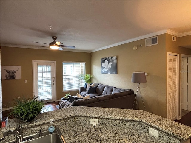 living room featuring wood finished floors, a ceiling fan, visible vents, and ornamental molding