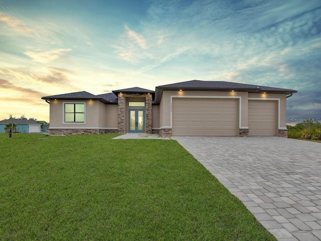 prairie-style home with stucco siding, a front lawn, decorative driveway, stone siding, and an attached garage