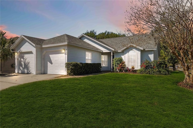 ranch-style home featuring a yard, driveway, a shingled roof, and a garage