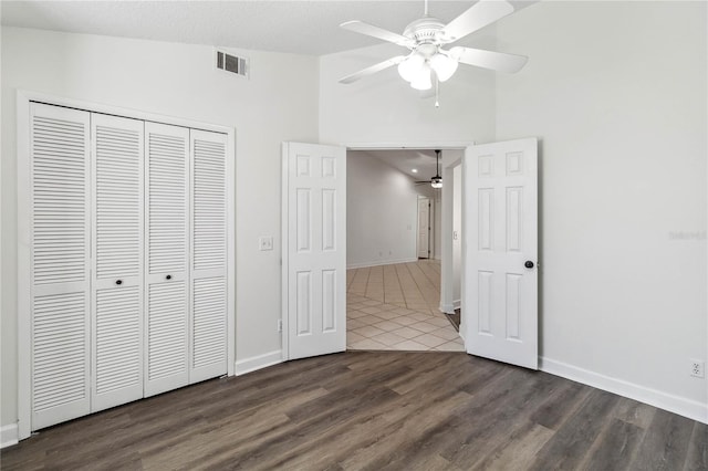 unfurnished bedroom with dark wood-style flooring, visible vents, high vaulted ceiling, baseboards, and a closet