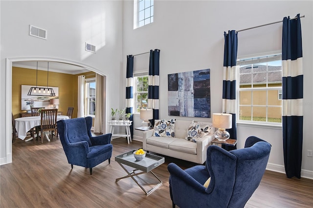 living area with wood finished floors, arched walkways, visible vents, and baseboards
