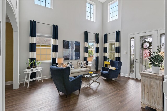 living area with arched walkways, a towering ceiling, baseboards, and wood finished floors