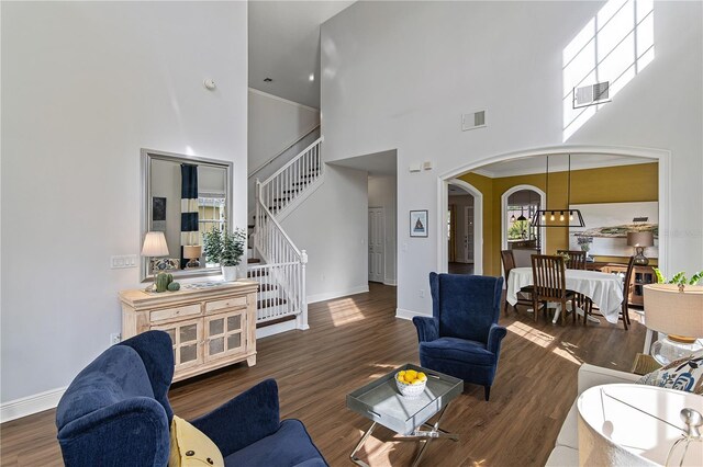 living room with visible vents, stairs, a high ceiling, wood finished floors, and arched walkways