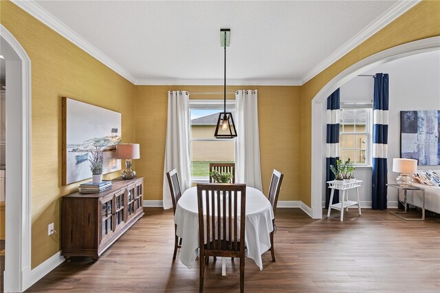 dining space featuring crown molding, wood finished floors, arched walkways, and baseboards