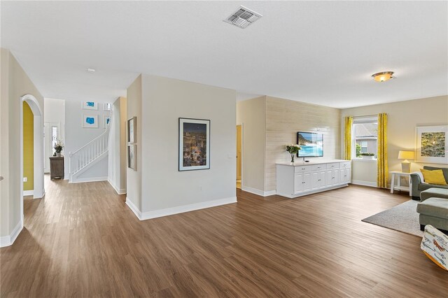 unfurnished living room with visible vents, dark wood-style floors, arched walkways, baseboards, and stairs